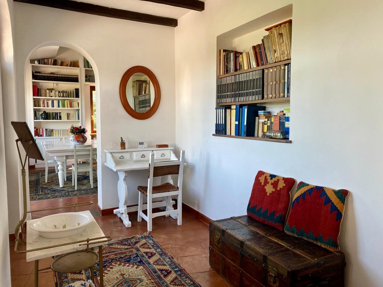 Angolo studio con scrivania bianca, specchio ovale e libreria a nicchia