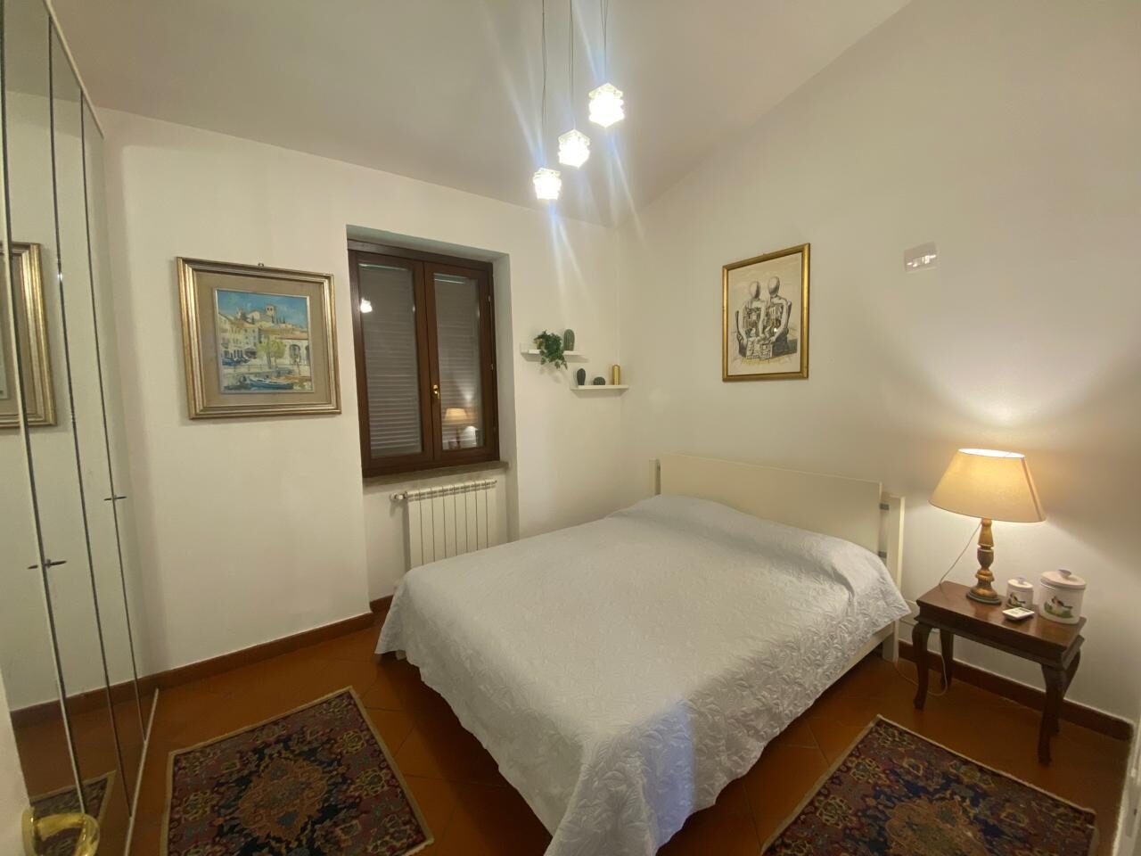 Camera matrimoniale bianca con abat-jour e finestra sulla campagna