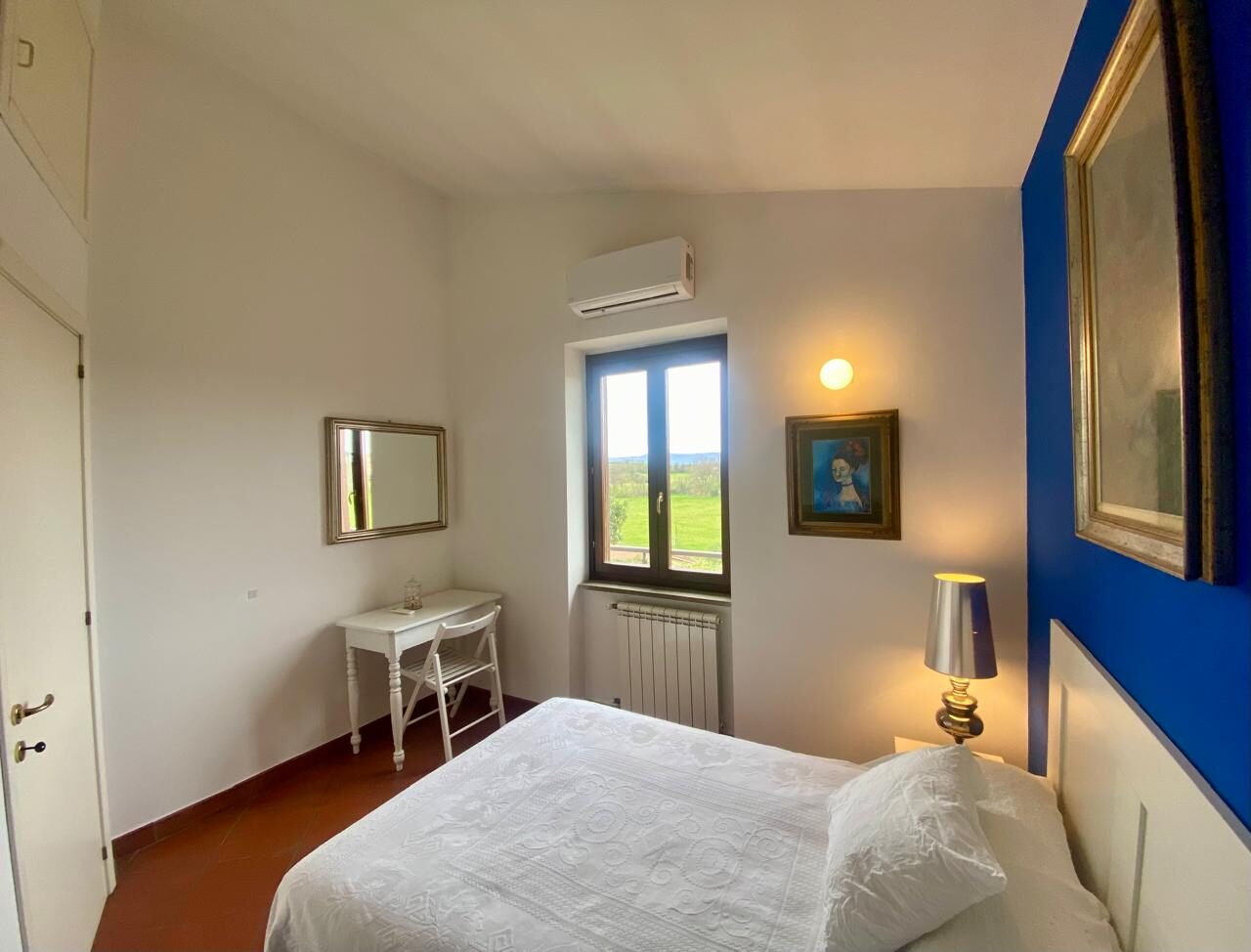 Camera da letto con parete blu, letto bianco e finestra sul verde