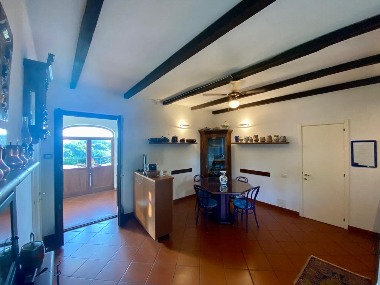 Sala con travi a vista, tavolo rotondo e porta ad arco sulla terrazza