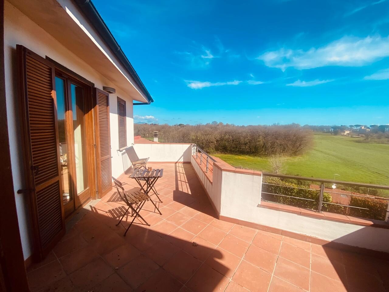 Terrazza con persiane in legno e tavolino, campagna di Nepi sullo sfondo